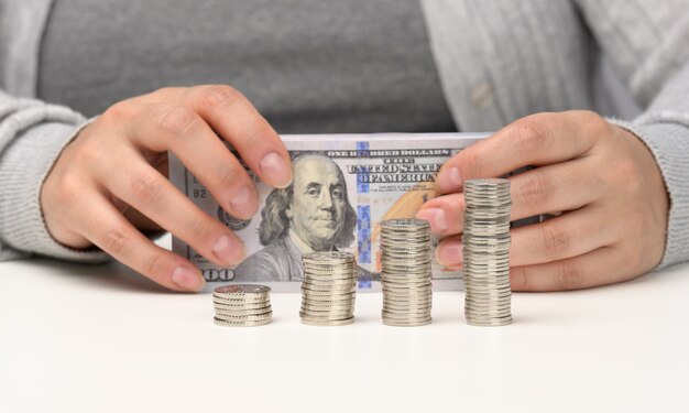 Pila de monedas en chtoli blanco y manos femeninas están sosteniendo una pila de dólares estadounidenses de papel. El concepto de control presupuestario, acumulación, obtención de beneficios.