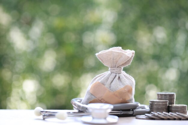 Foto una pila de monedas dinero y bolsa de dinero con estetoscopio en fondo verde ahorrar dinero para el concepto de seguro médico y atención médica