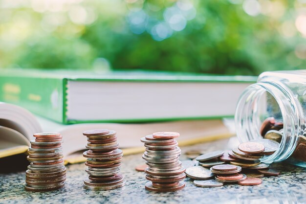 Pila de monedas de dinero en el frasco de vidrio con libros sobre fondo verde natural borrosa