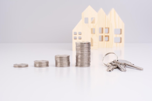 Una pila de monedas y una llave en un fondo gris con una casa modelo con reflejo