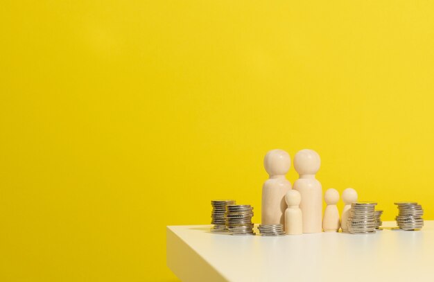 Pila de monedas de metal y figuras de madera de hombres sobre una mesa blanca. Ahorros y gastos, presupuesto familiar, subsidios del estado