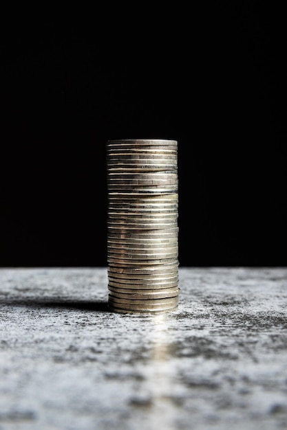 Pila de monedas sobre mesa gris y fondo negro