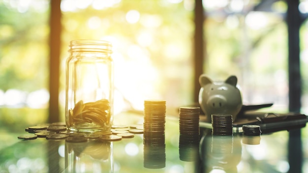 Pila de monedas, un tarro de dinero de vidrio y una alcancía sobre la mesa para el ahorro y el concepto financiero