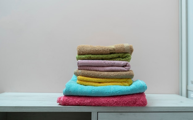 Una pila de nuevos textiles de toallas limpias y frescas de color en el estante de la lavandería
