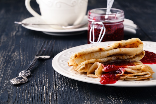 Pila de panqueques americanos o buñuelos con mermelada de fresa y arándano en plato blanco sobre mesa rústica de madera