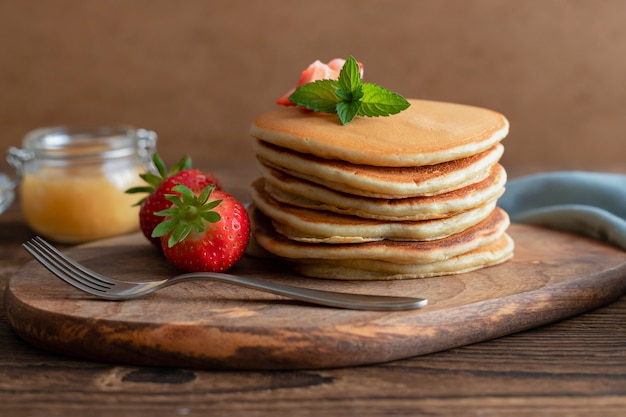 Foto una pila de panqueques americanos sobre una tabla de madera con miel y bayas para el desayuno o el postre