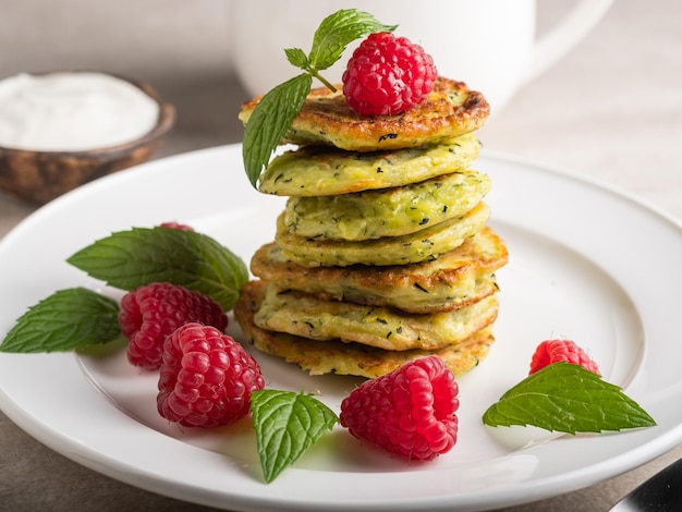 Pila de panqueques de calabacín caseros frescos cubiertos con frambuesas y crema agria. Té verde