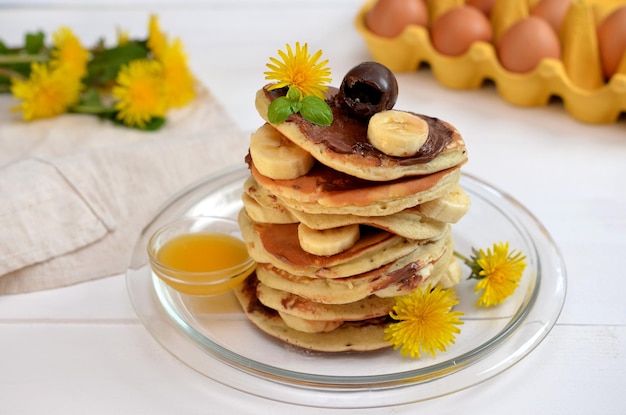 Pila de panqueques con chocolate y plátano y flores de primavera