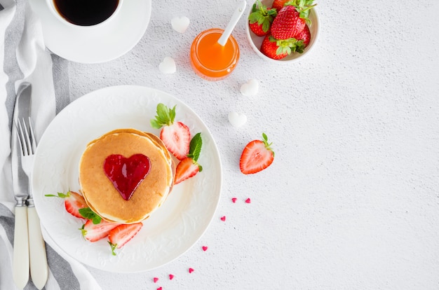 Una pila de panqueques con un corazón de mermelada encima con fresas frescas