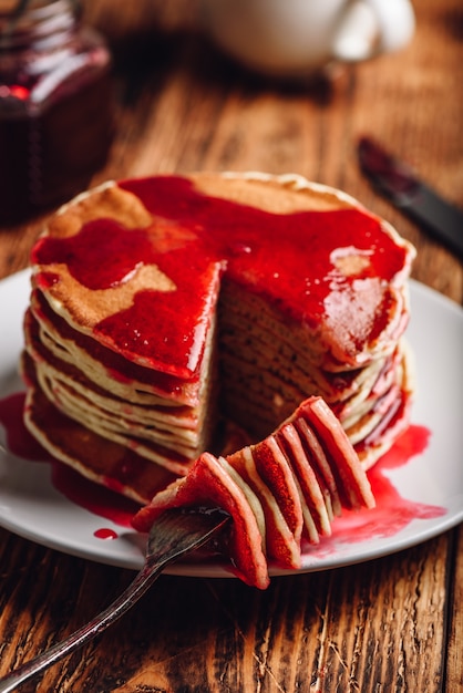 Pila de panqueques con mermelada de frutos rojos en placa sobre superficie de madera