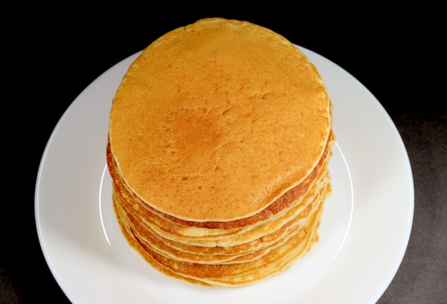 Pila de panqueques recién hechos en plato blanco sobre fondo negro