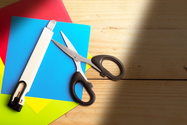 Foto pila de papel de colores con tijeras y cortador con fondo de madera