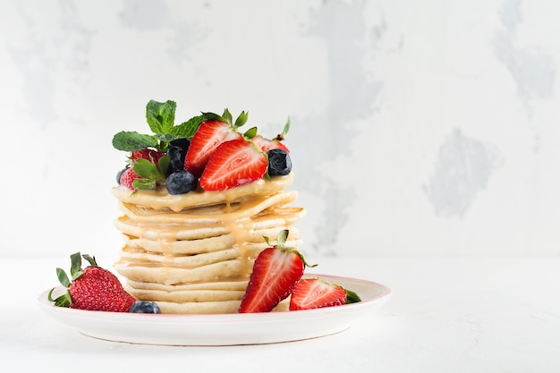 Pila de pequeños panqueques caseros con miel, fresas frescas y salsa