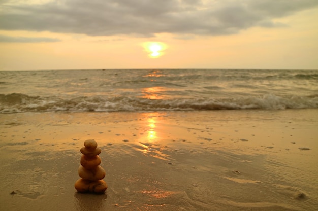 Pila de piedras de guijarros equilibradas en la playa de la puesta del sol contra las olas salpicadas