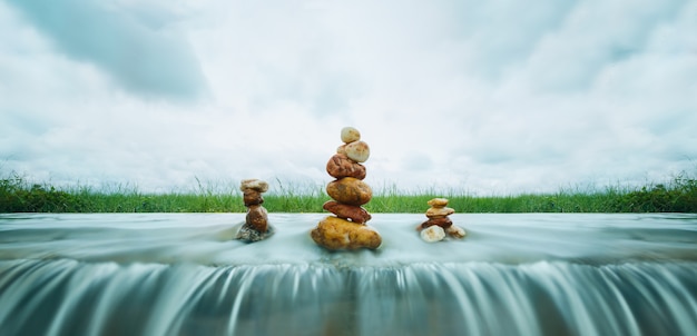 Pila de piedras zen sobre cascada sobre fondo de tormenta de nubes
