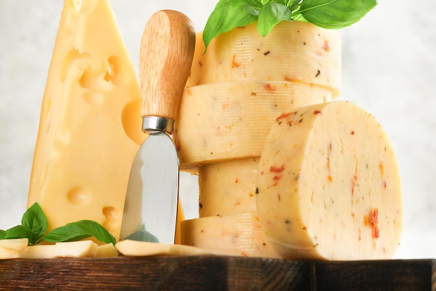 Pila de queso con tomates y condimentos y queso suizo con albahaca y cuchillo en una tabla para servir sobre fondo de mesa gris claro Surtido de diferentes tipos de queso Fondo de queso