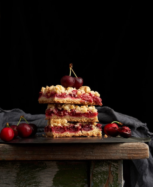 Pila de rebanadas cuadradas de un pastel con cereza roja, fondo negro