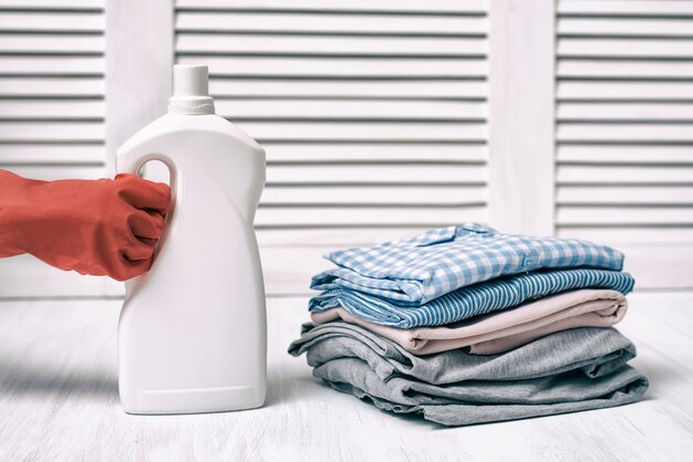 Pila de ropa doblada y botella de detergente en mano femenina. Tareas del hogar