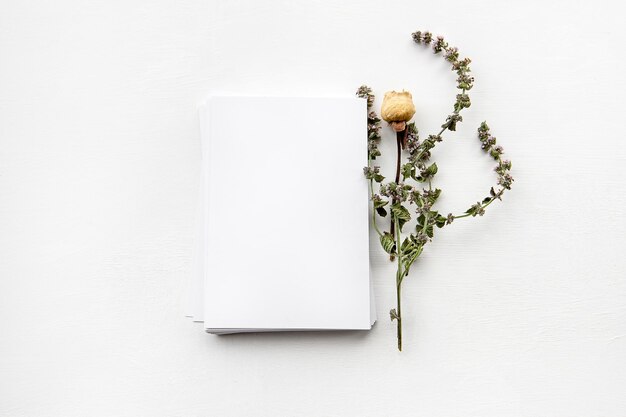 Una pila de tarjetas y flores vacías en una mesa blanca en blanco para una postal