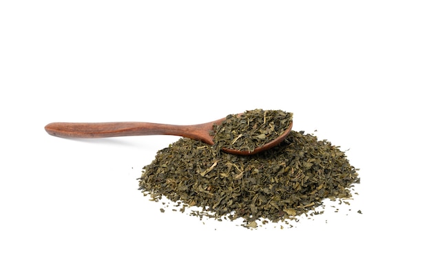 Pila de té verde seco y cuchara de madera marrón aislado