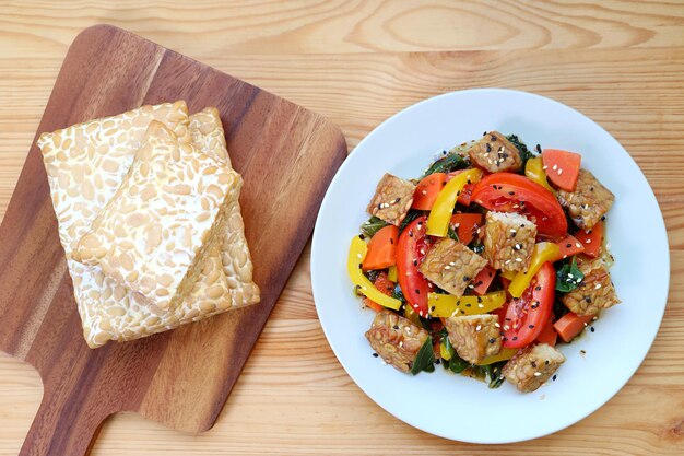 Pila de Tempeh fresco y ensalada de verduras coloridas con cubos de Tempeh asado sobre mesa de madera