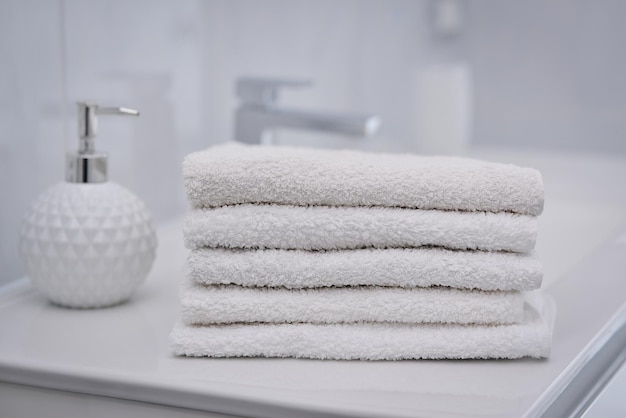 Pila de toallas blancas dobladas sobre fondo de baño borroso
