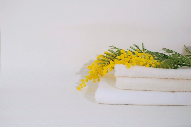 Pila de toallas blancas limpias en la mesa del baño con flores de mimosa. Toallas blancas sobre una mesa blanca con espacio para copiar.