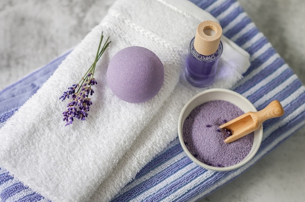 Pila de toallas limpias y suaves con un montón de lavanda, sal de baño y ambientador en gris claro.