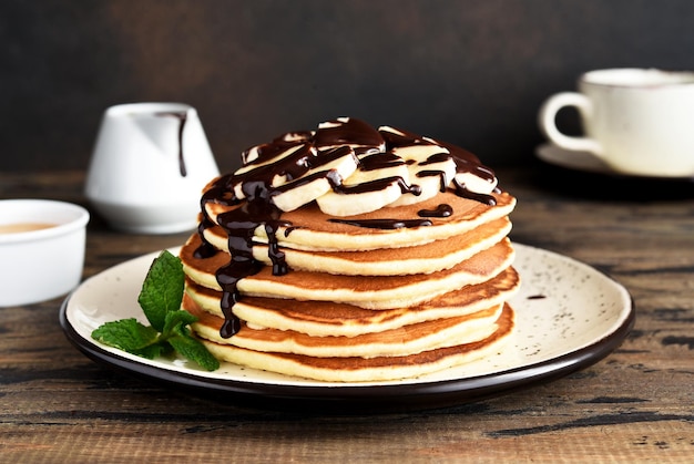 Pila de tortitas con plátano y salsa de chocolate sobre fondo marrón de madera