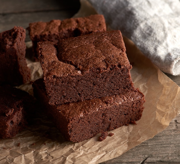 Pila de trozos cuadrados horneados de pastel de brownie de chocolate en papel pergamino marrón