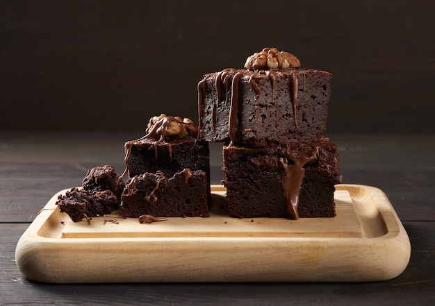 Pila de trozos horneados de pastel de chocolate brownie con nueces sobre una tabla de madera, delicioso postre, de cerca