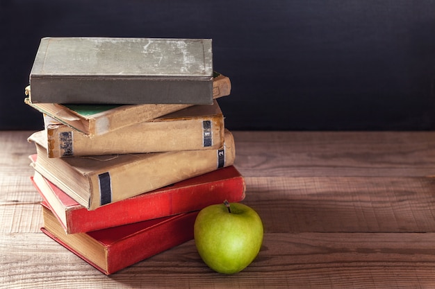 Una pila de viejos libros antiguos y una manzana verde sobre una rústica mesa de madera.