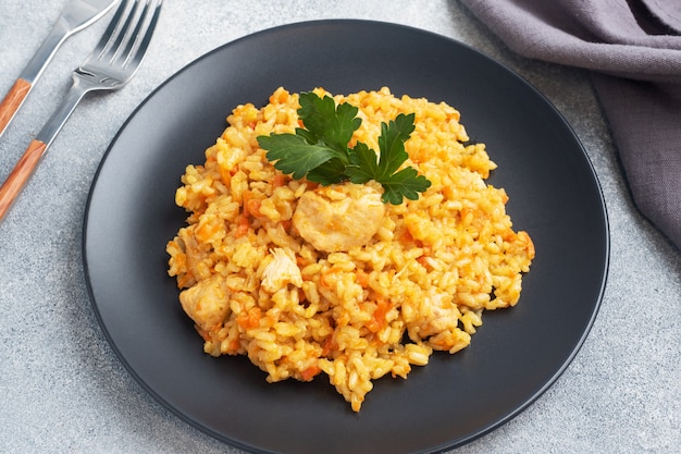 Pilaf asiático delicioso, arroz guisado con verduras y pollo en un plato. Fondo de hormigón gris.