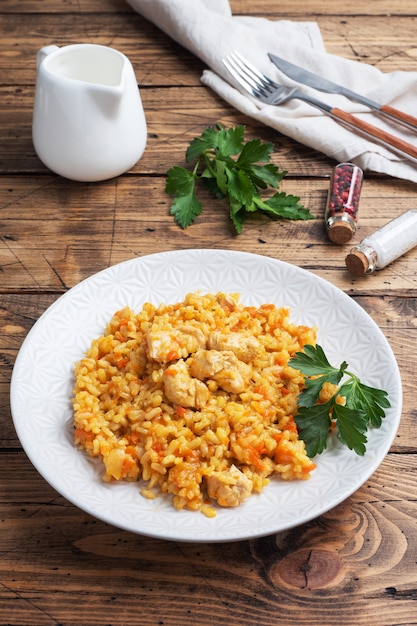 Foto pilaf asiático delicioso, arroz guisado con verduras y pollo en un plato. fondo rústico de madera.