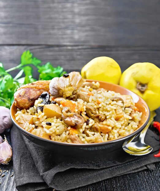 Pilaf aus Reis, Ente, Quitte, Karotten mit Knoblauch, Zwiebeln, Pflaumen und Gewürzen in einem Teller auf einer Serviette auf schwarzem Holzbretthintergrund