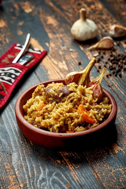 Pilaf clásico con ajo de res y zanahorias en un plato de arcilla sobre un fondo de madera Rústico