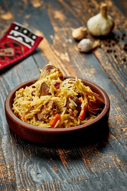 Pilaf clásico con ajo de res y zanahorias en un plato de arcilla sobre un fondo de madera Rústico