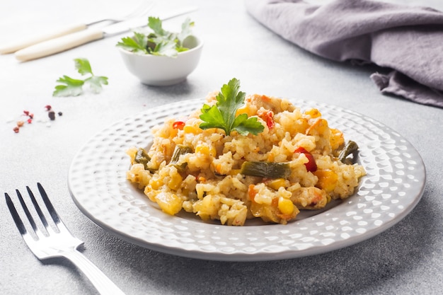 Pilaf com legumes e frango em um prato cinza em uma luz.