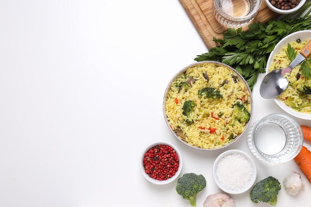 Pilaf in Schüsseln, Gewürze, Gemüse und ein Glas Wasser auf weißem Hintergrund, Platz für Text