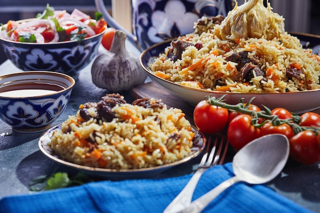 Pilaf uzbeko en un auténtico plato azul y dorado, filmado sobre un fondo azul con tomates, ajo y té