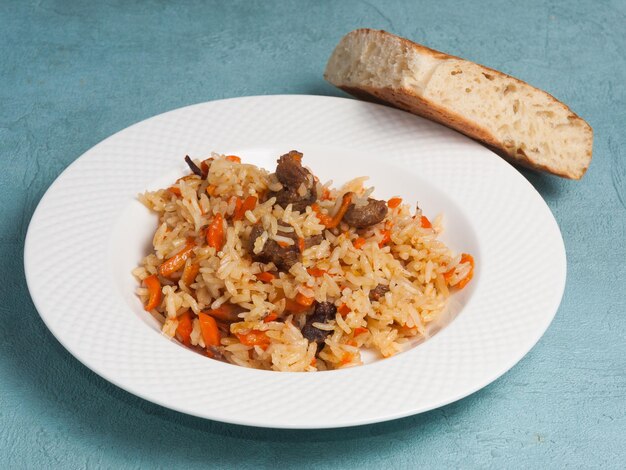 Pilaf uzbeko tradicional en un plato blanco sobre un fondo azul.