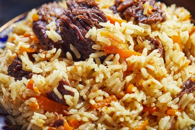 Pilaf uzbeque em um autêntico prato azul e dourado, filmado em um fundo azul com tomate, alho e chá