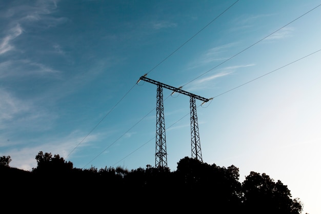 Pilão de transmissão de eletricidade em silhueta contra o céu azul