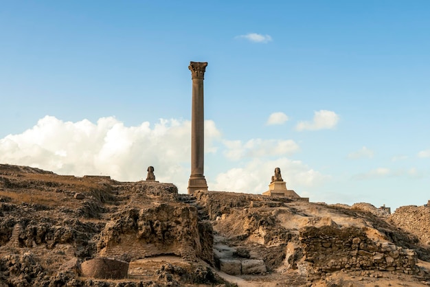 Pilar de Pompeyo Columna antigua y esfinge en la colina contra el fondo de un cielo azul nublado Alejandría Egipto