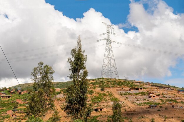 Foto pilares de electricidad instalados en un área rural con casas construidas en una colina en el fondo