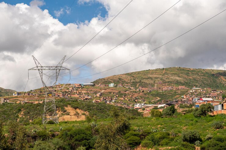 pilares de electricidad instalados en un área rural con casas construidas en una colina en el fondo