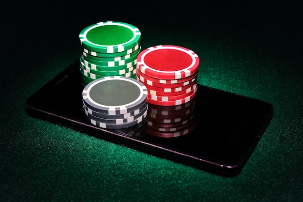 Pilas de fichas de casino en un teléfono inteligente, fondo de mesa de póquer de fieltro verde. Concepto de juego online.