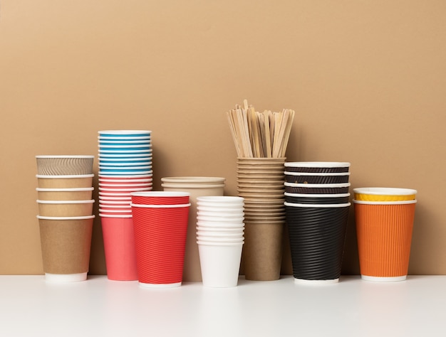 Pilas de vasos de papel desechables surtidos para bebidas, café y té en una mesa blanca. Envase de bebida para llevar