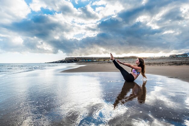 Pilates fitness cuida el descanso corporal y la posición de permanencia para una joven mujer caucásica en la orilla de la playa imagen escénica para el concepto de salud corporal yoga equilibrado en contacto y sentimiento con la naturaleza
