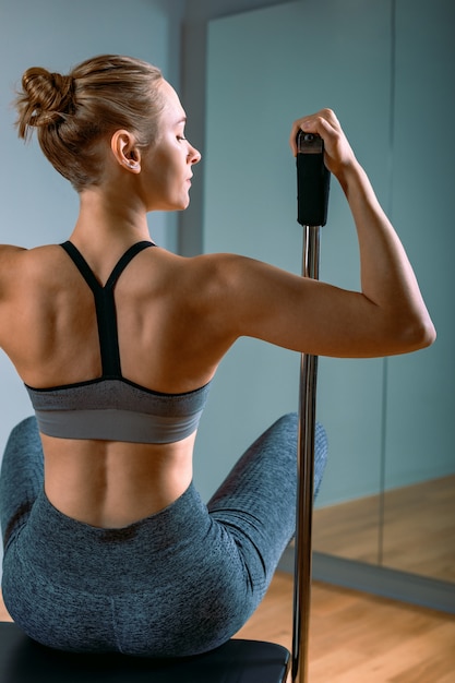 Pilates-Frau in einem Cadillac-Reformer, der Dehnungsübungen im Fitnessstudio macht